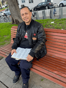 A man sits on a park bench reading an open book.