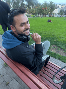 A man sits on a park bench, looking over his shoulder and smiling.