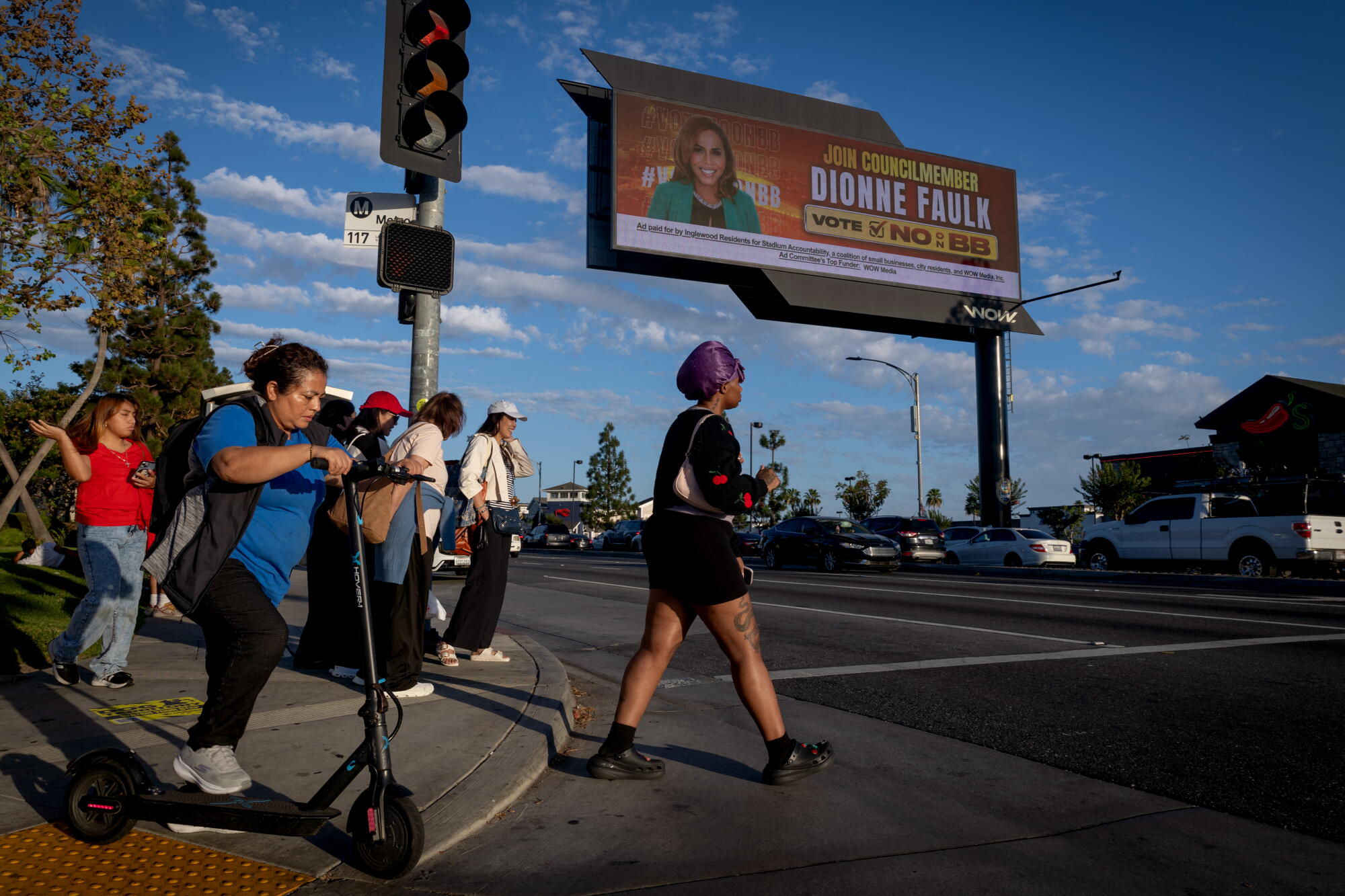 People cross Century Boulevard near an electronic billboard in Inglewood.
