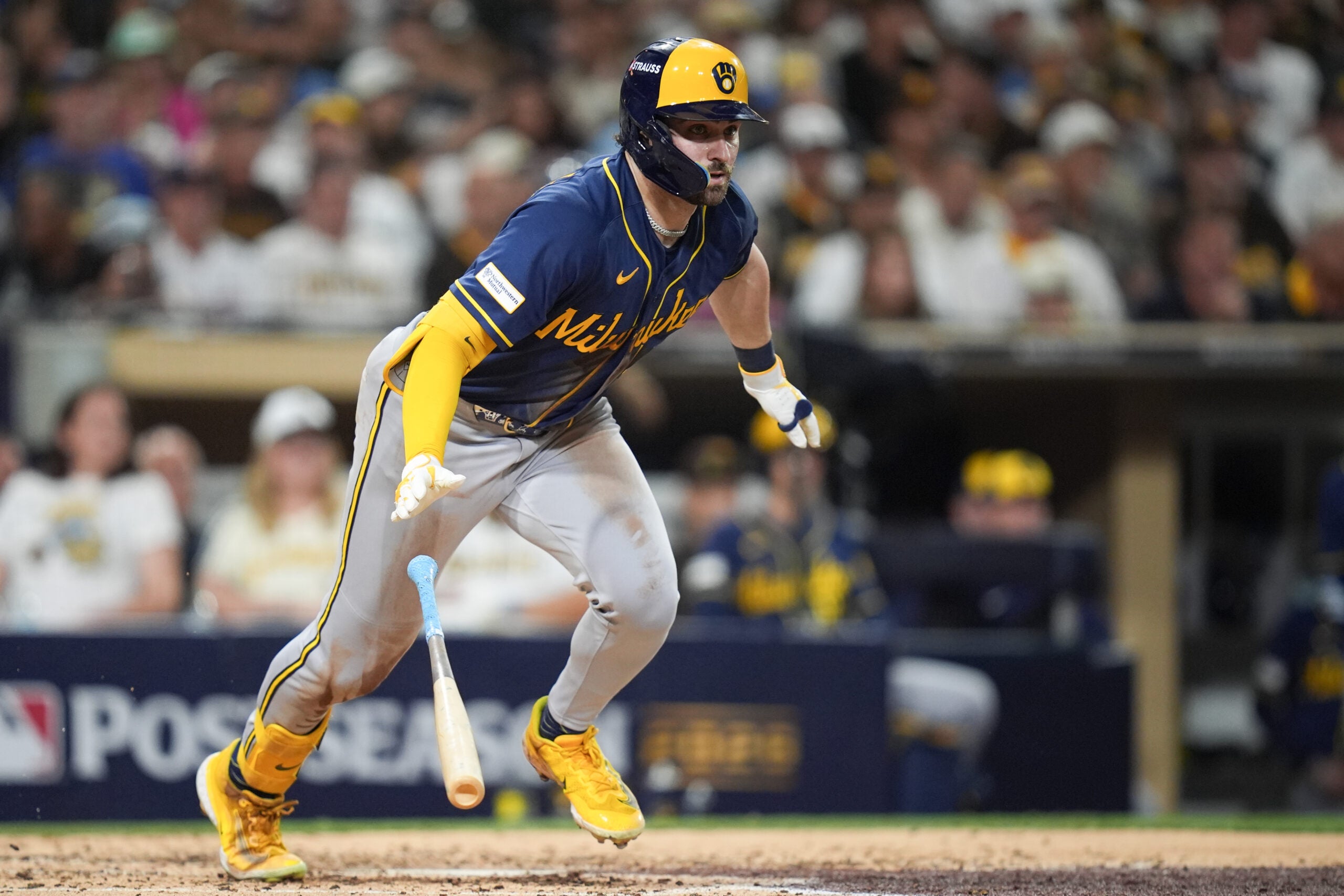 A Milwaukee Brewers baseball player in a blue and yellow uniform running toward first base while dropping his bat.