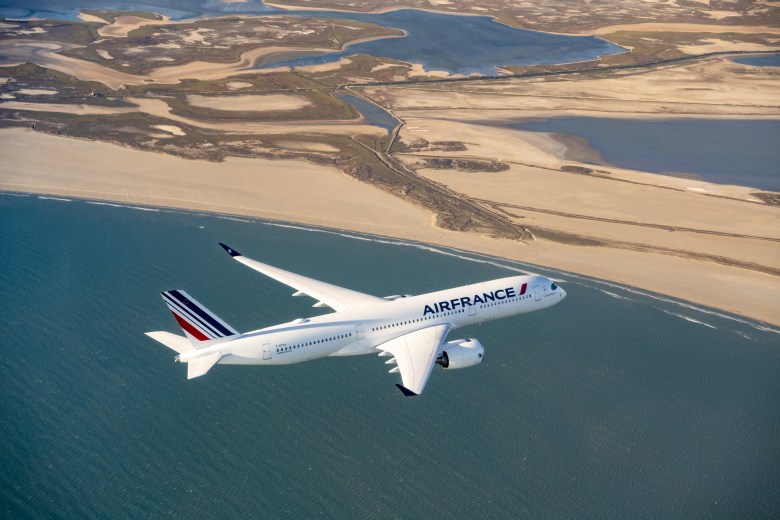 an airliner in the skies over water and near land. The plane bears the insignia "Air France."