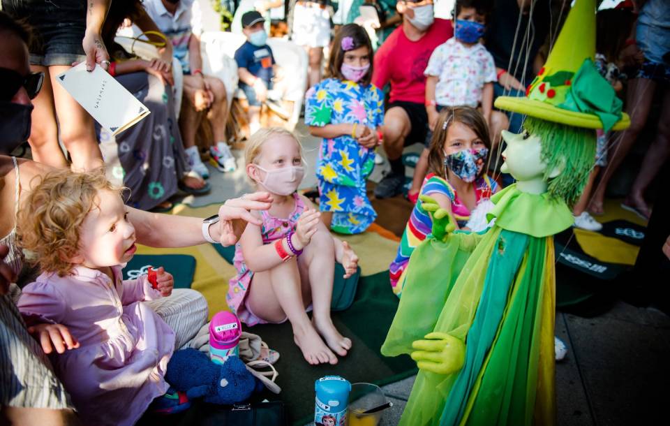 small children watch a green witch puppet