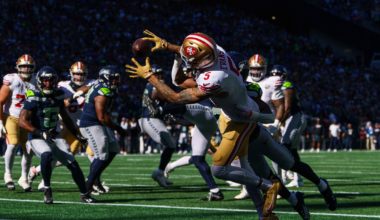 A San Francisco 49ers player leaps to catch a football while a Seattle Seahawks defender closely guards him near the end zone during a game.