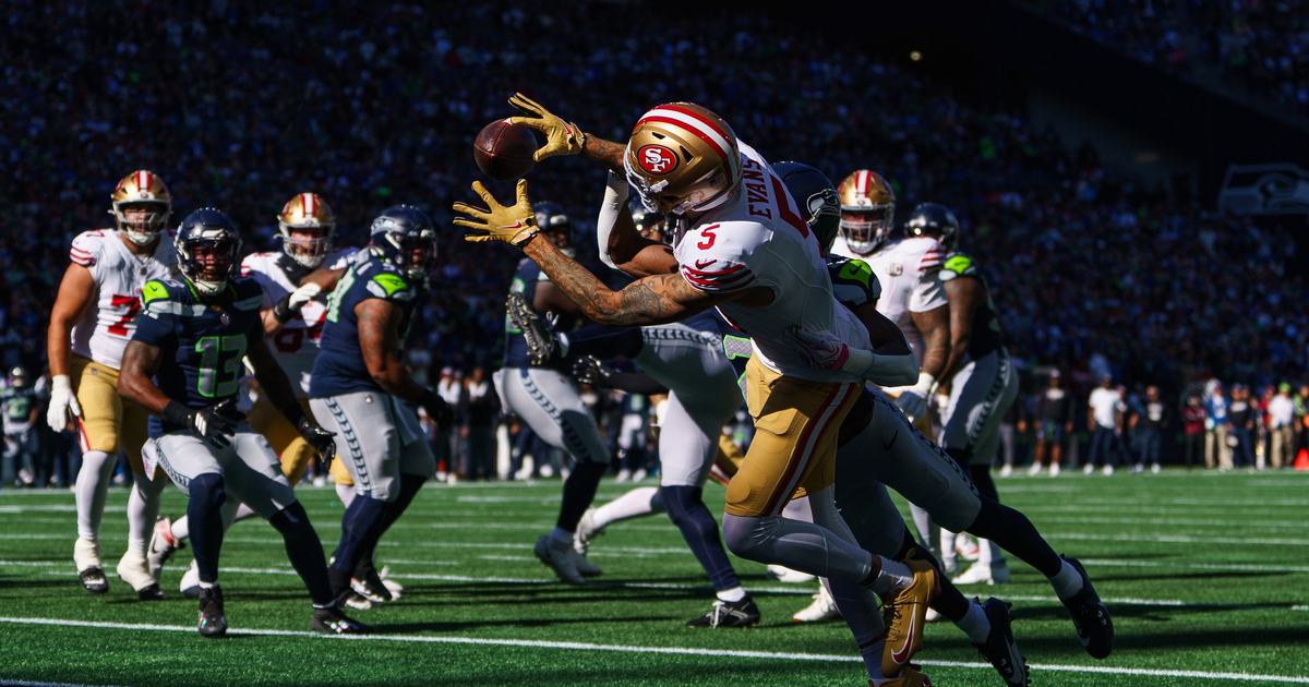 A San Francisco 49ers player leaps to catch a football while a Seattle Seahawks defender closely guards him near the end zone during a game.