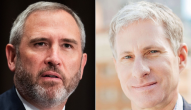 A man with short gray hair and beard wears a suit and tie, while another clean-shaven man with light hair smiles wearing a checked shirt and blazer.