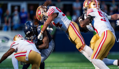 A Seattle Seahawks player is tackled by three San Francisco 49ers defenders during an intense football game on a sunlit field.
