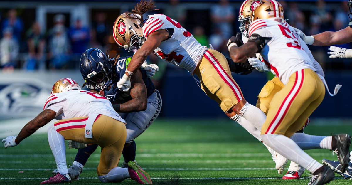 A Seattle Seahawks player is tackled by three San Francisco 49ers defenders during an intense football game on a sunlit field.