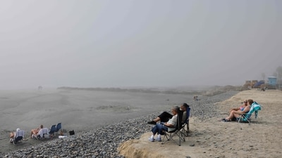 People sit (R) on what remains of an eroded beach as work continues on a sand replenishment project nearby along the Pacific Ocean shoreline in Oceanside, California. (Getty Images via AFP)