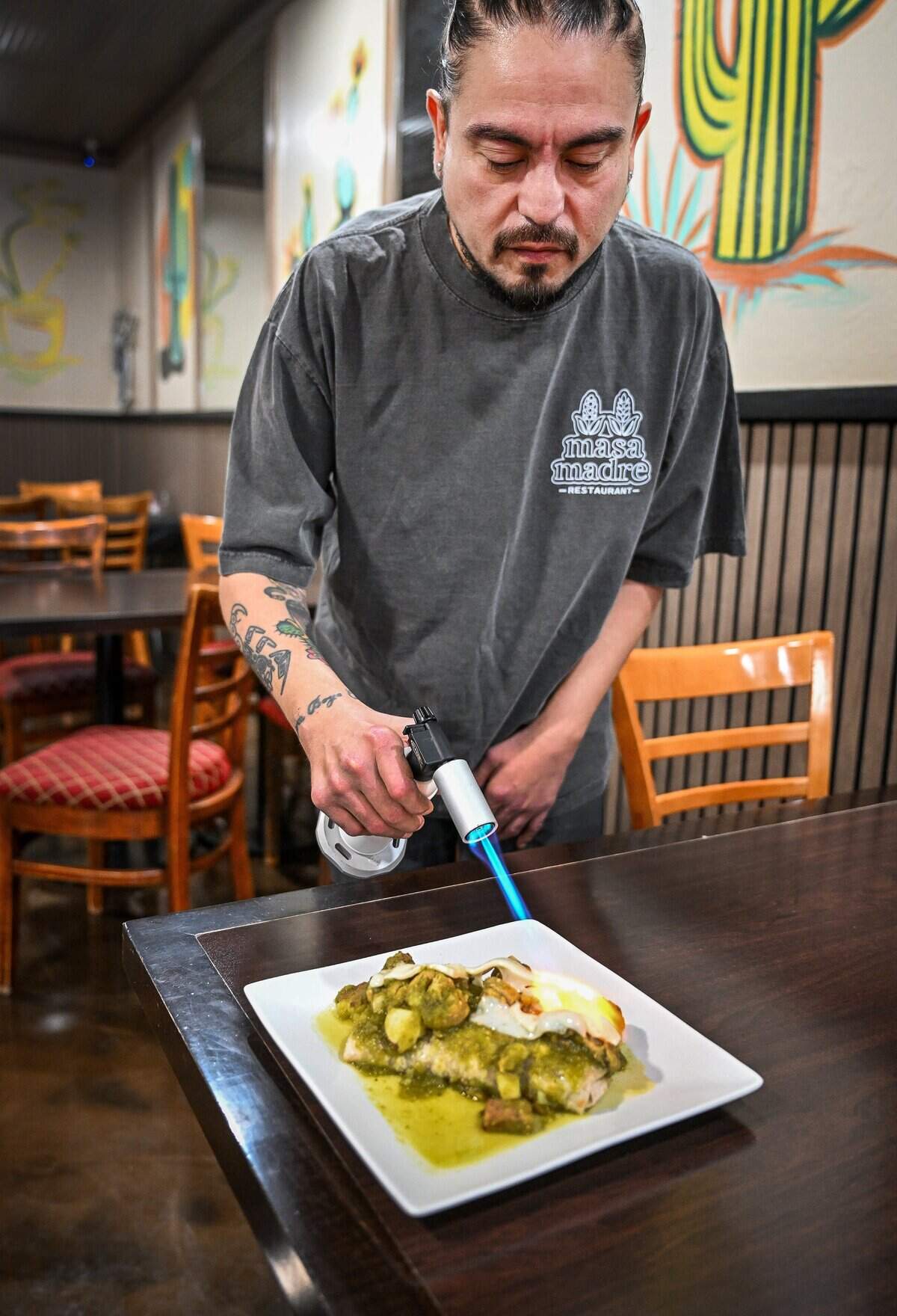 Bryan Hernandez shows how he will use a flame torch to melt and char the cheese on a chili verde burrito table side at his new restaurant, Masa Madre, on the northeast corner of Palm and Bullard in Fresno.