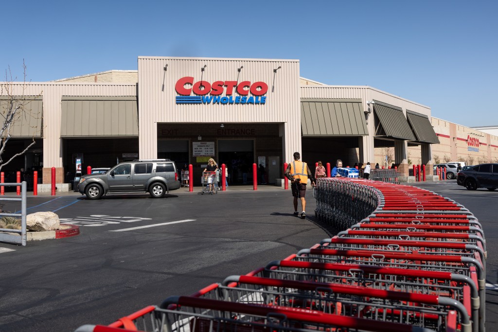 Exterior view of a Costco Wholesale warehouse with a long line of shopping carts curving in the foreground.