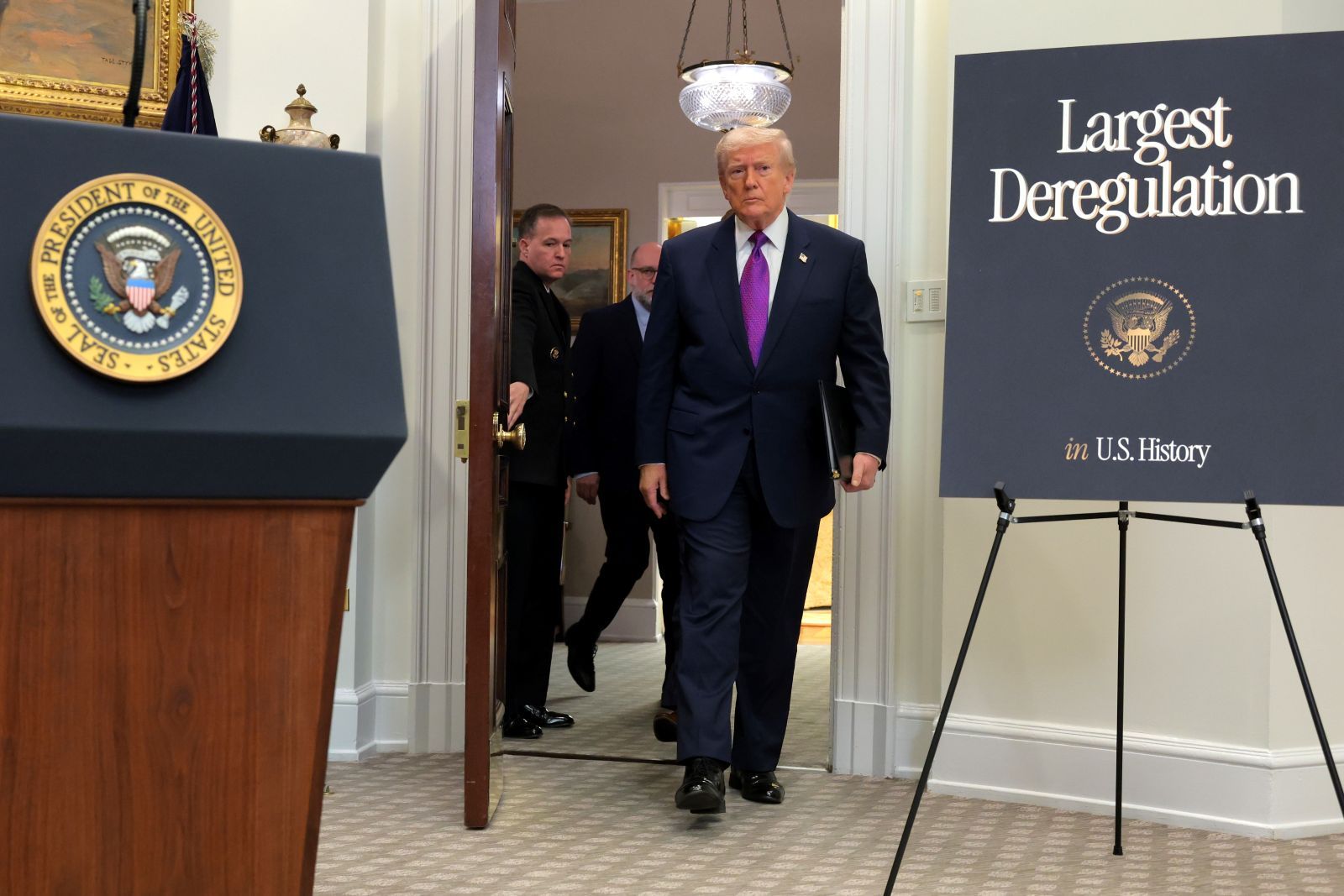President Donald Trump emerges for a press conference next to a sign reading Largest Deregulation in US History