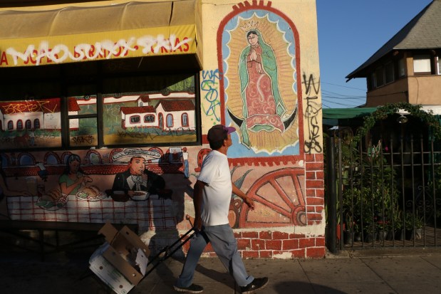A passerby gazes up at a Virgin of Guadalupe mural on a building in Boyle Heights in this image by Sam Quinones. It's from his book "Our Lady of the Angels: The Virgin of Guadalupe on the Walls of Los Angeles." (Courtesy Angel City Press)