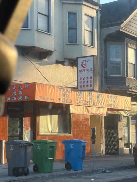 Exterior of TF Restaurant with Chinese signage, an orange awning, and three trash bins on the sidewalk.