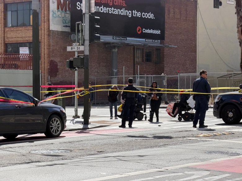 Police officers stand behind yellow caution tape at an urban intersection with a CodeRabbit billboard in the background.