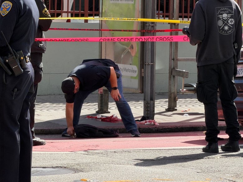 Police officers investigate a crime scene cordoned off with tape on a city sidewalk.