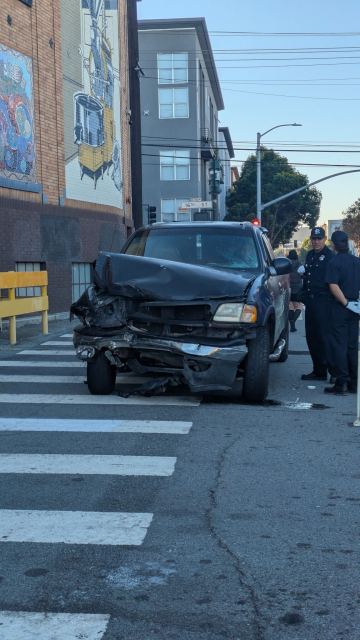 A pickup truck with significant front-end damage stopped on a crosswalk next to two police officers.