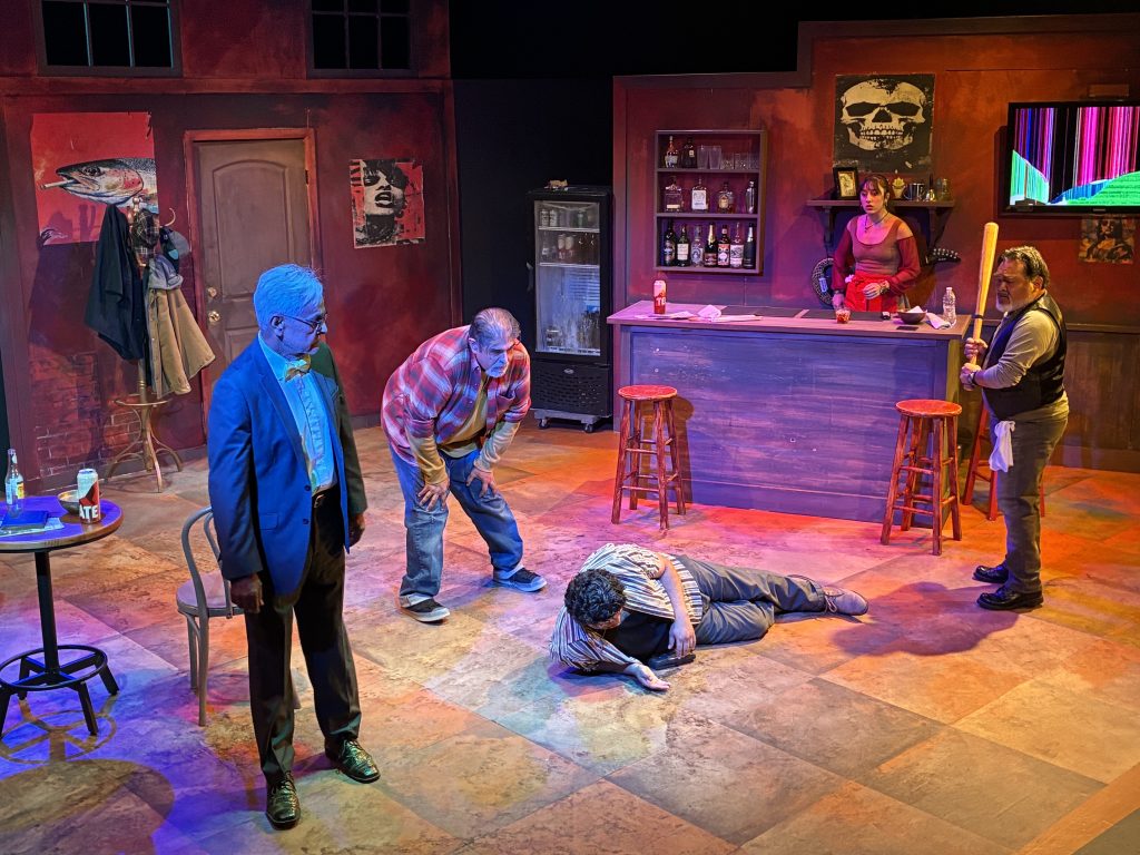A dramatic scene from Dive Bar at CASA 0101 Theater shows a man collapsed on the floor as other characters react.