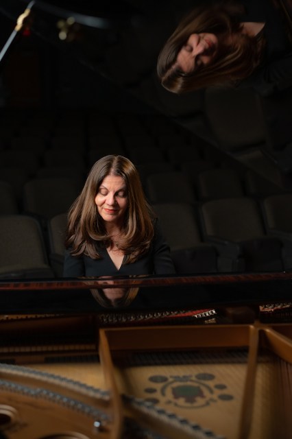 A woman plays a grand piano in a darkened auditorium.