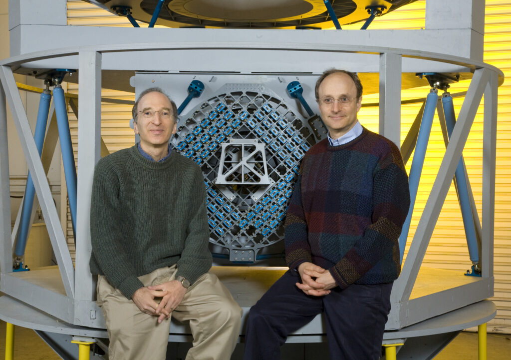 two men posing in front of a blue apparatus