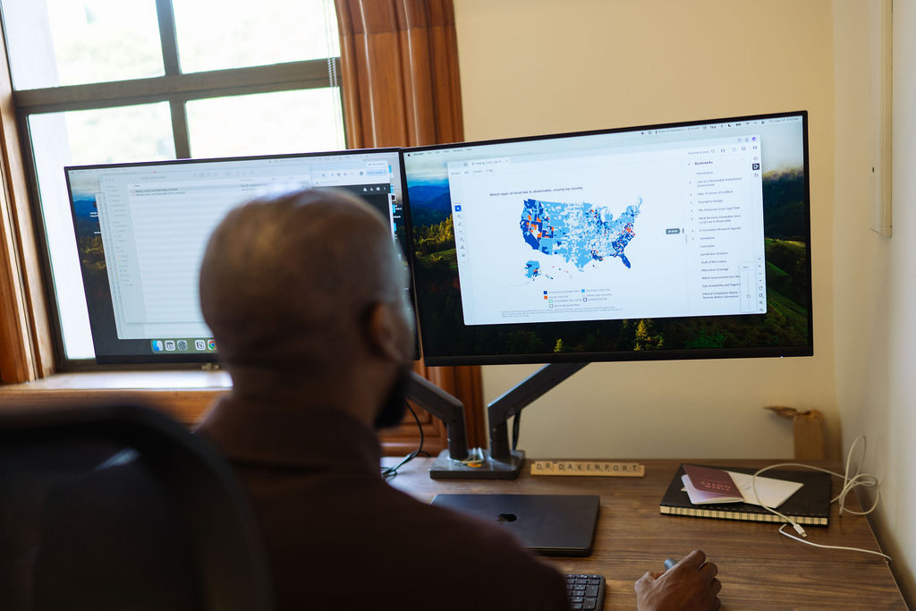 A view of Diag Davenport's shoulder as he scrolls on a computer screen across a map of the U.S. that contains different shades of blue. The coloring illustrates the different types of laws across the country, as captured in the dataset he and a team produced and made public.