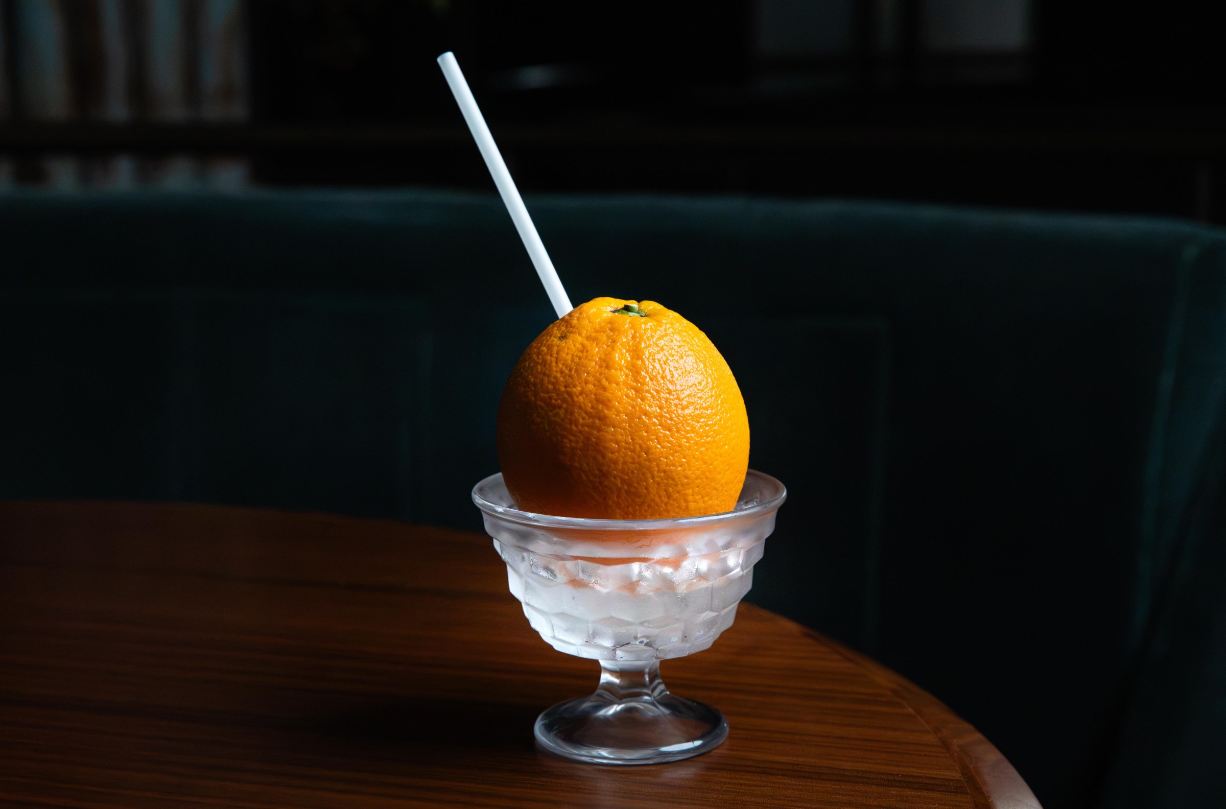 A footed pedestal cup with an orange and a straw struck through it at Shinka in San Francisco.