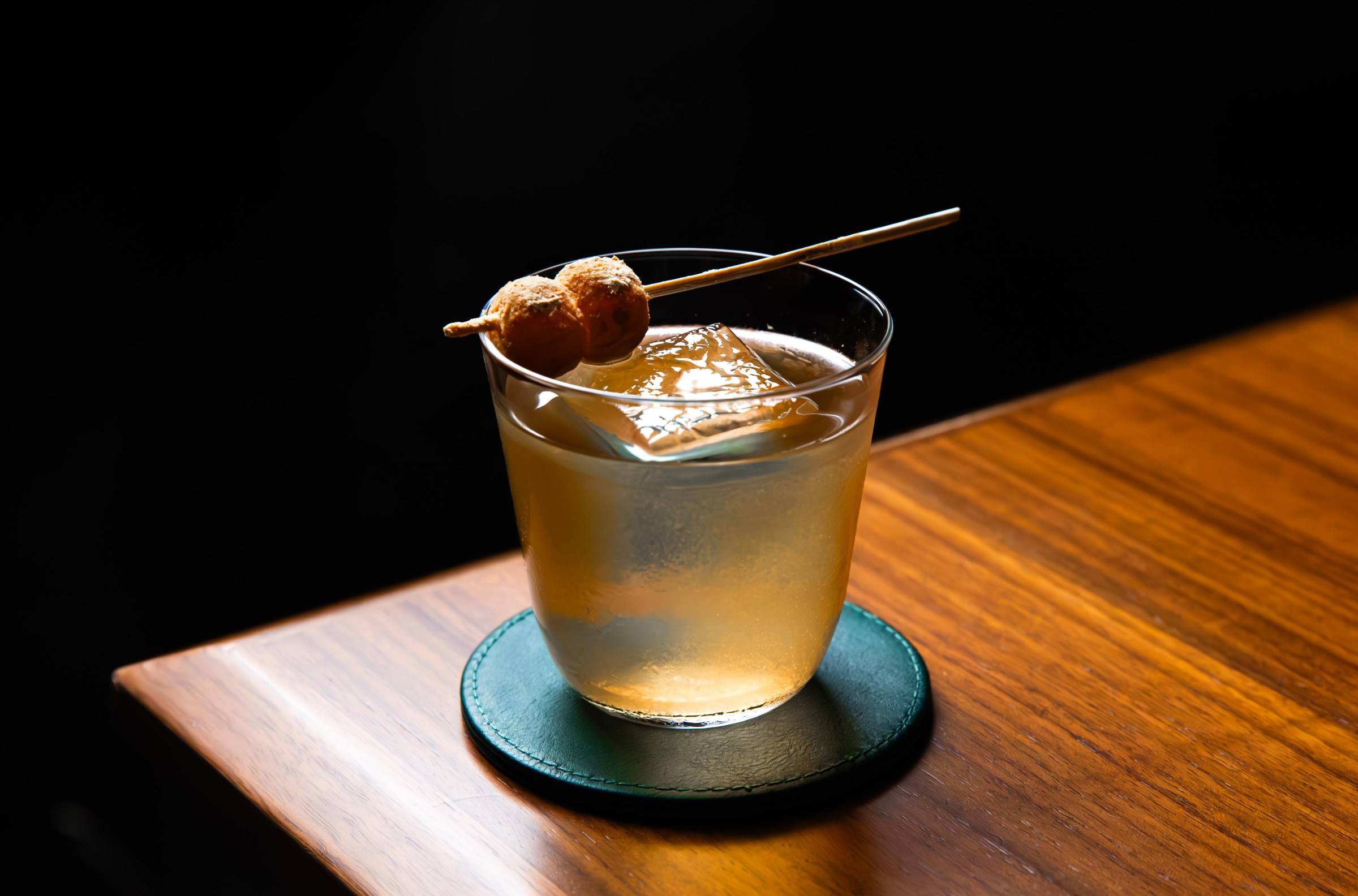A cocktail glass with an amber liquid and a garnish on a toothpick at Shinka in San Francisco.