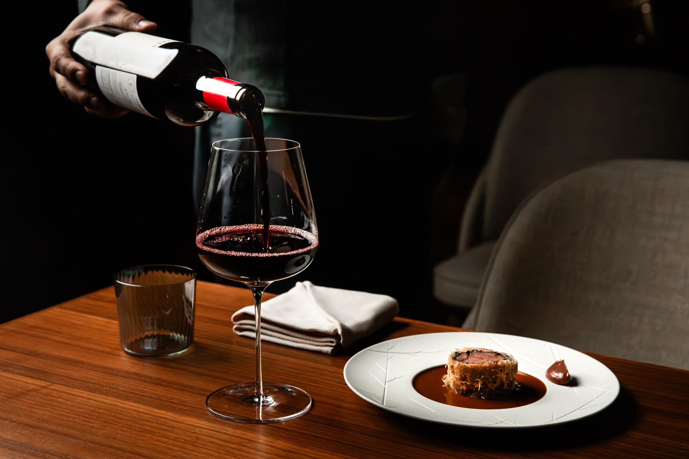 Wine is poured into a wine glass next to a plate with food on it at Shinka in San Francisco.