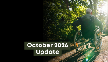 A wheelchair user travels along a tree-lined path in a public park as sunlight filters through the surrounding trees, the text on top reads