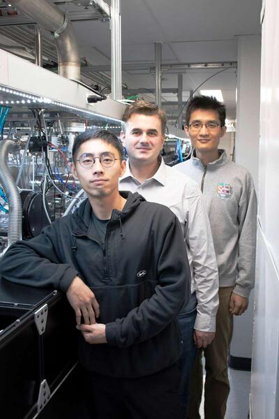 Three scientist standing in a lab next to equipment.