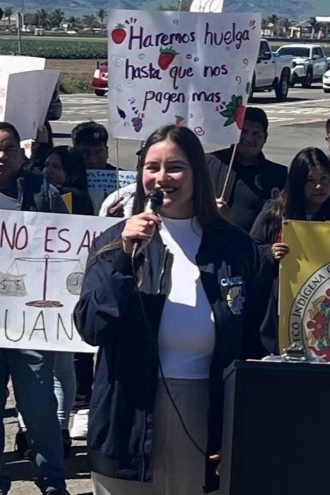 Hazel Davalos speaks in front of a crowd of demonstrators with handwritten Spanish posters calling for fair wages