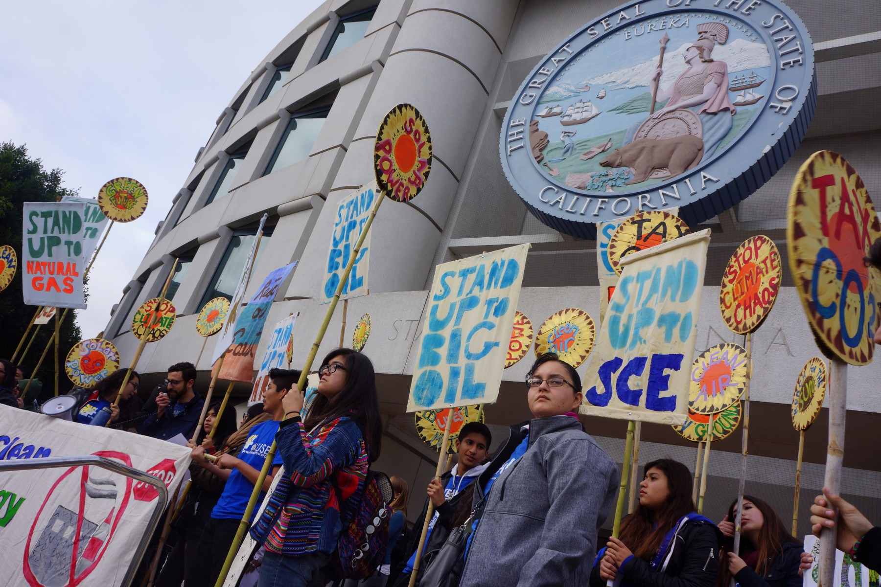 Youth at a protest hold handpainted banners reading 'Stand Up to Big Oil' and 'Stop Climate Chaos'
