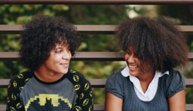 Two Black teens lean against a metal fence and smile at each other