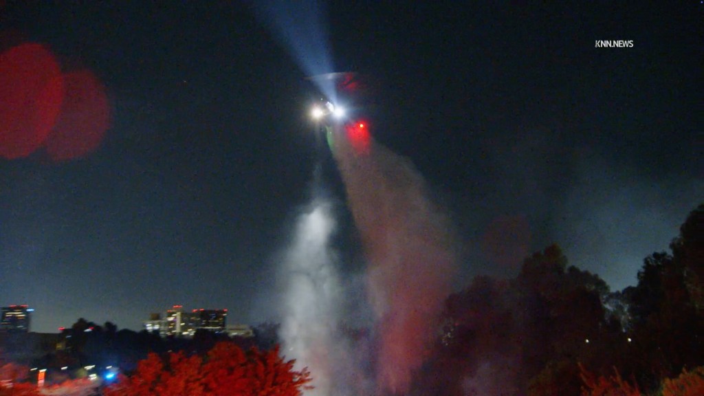 A helicopter drops water on a brush fire at night near the Department of Veterans Affairs West Los Angeles Campus.