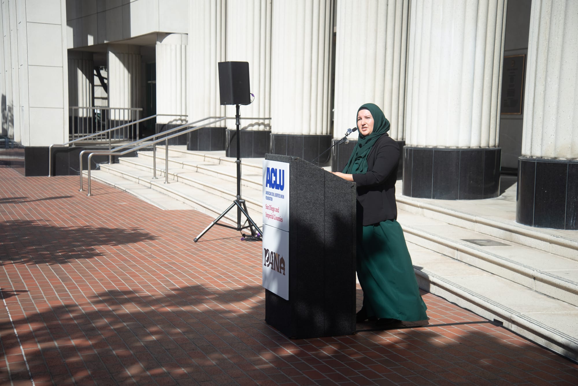 A woman in a green hijab stands at a podium.