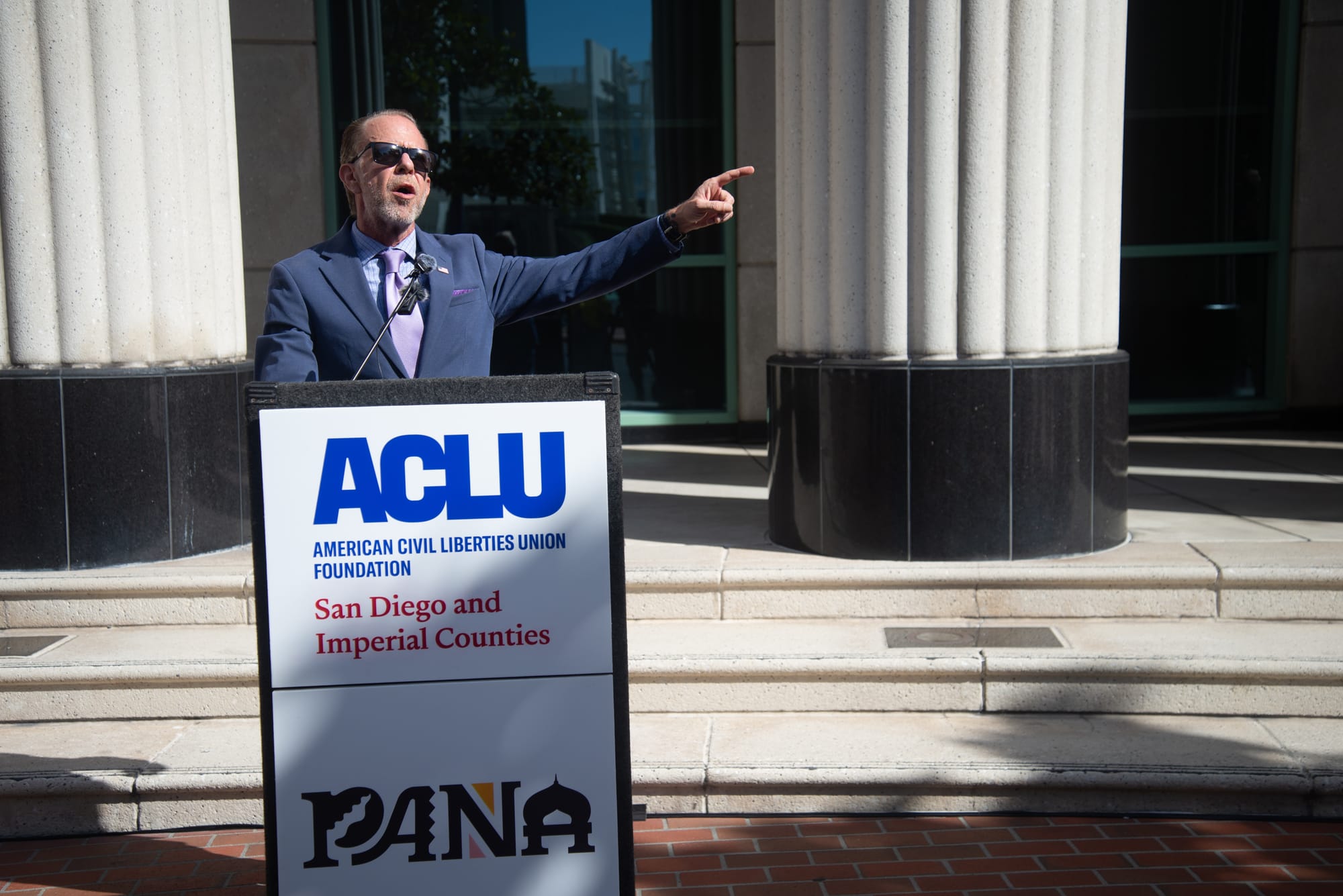 A man in a gray suit stands at a podium.