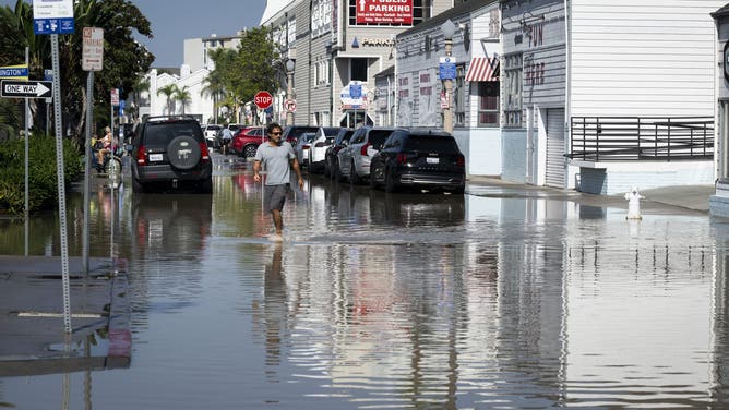 NEWPORT BEACH, CA - October 09: A man crosses E. Bay Ave on the Balboa Peninsula after high tides flooded streets in Newport Beach on Friday, October 9, 2026.