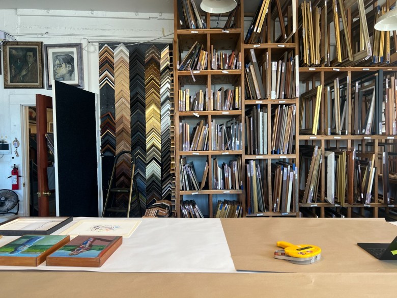Custom picture framing shop with walls of stacked frame samples and shelves filled with various wooden and metal frames.