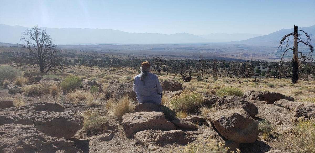 A man sits on a rock in an arid, hilly environment.