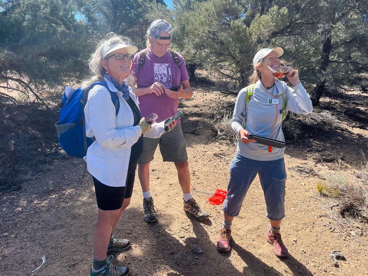 Three people stand outdoors in an arid, shrub filled environment.