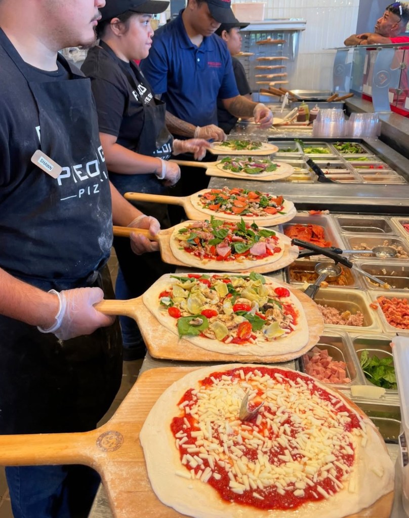 Employees preparing pizzas in a restaurant line.