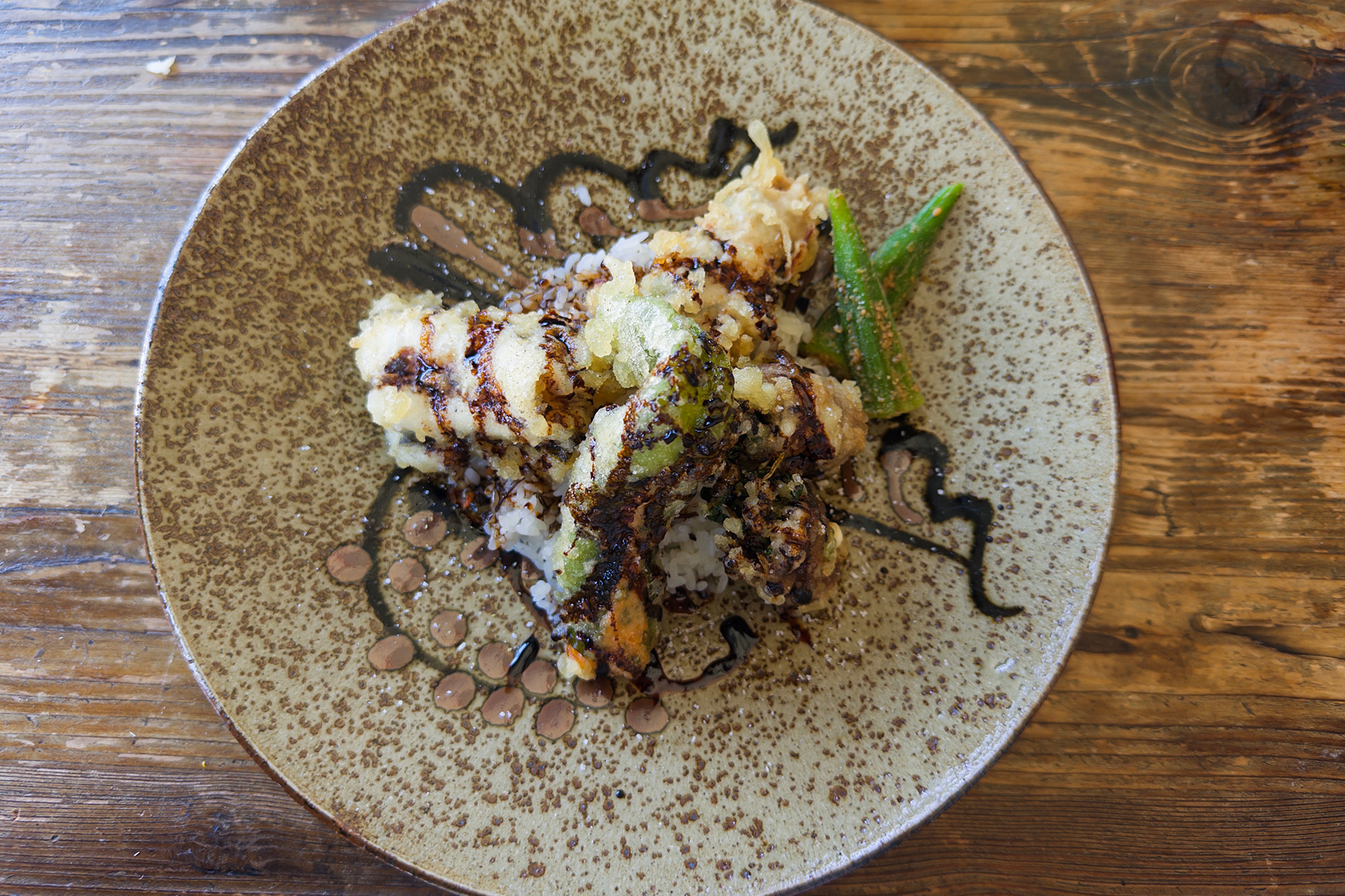 Overhead view of a tempura rice bowl, artfully drizzled with thick soy sauce.