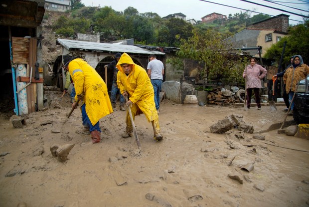 Two homes were partially destroyed after a hillside collapsed due to the heavy rains that began Monday afternoon. Residents help shovel out mud from the two properties in Colonia Artesanal on Tuesday, Feb. 6, 2024 in Tijuana, Baja California. (Alejandro Tamayo / The San Diego Union-Tribune)