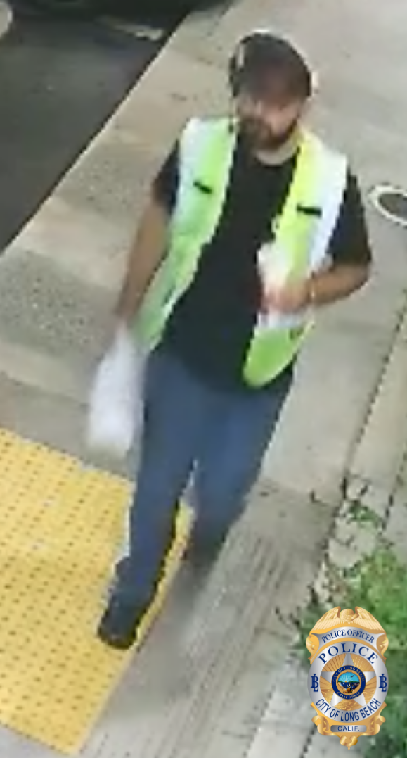 Blurry image of a man bearded man wearing a dark baseball cap, white headphones, black t-shirt, yellow reflective vest and blue pants.