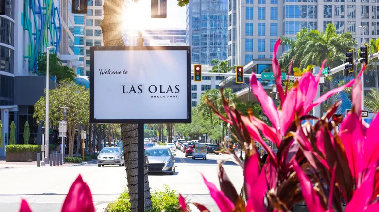 A sign that say Welcome to Las Olas Boulevard with foliage in the front and buildings in the back