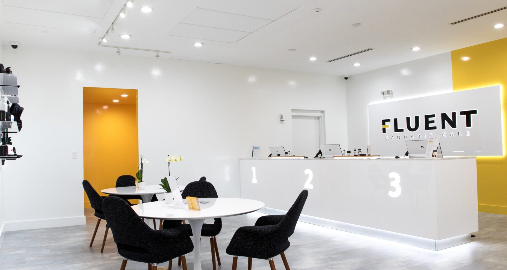 Inside Fluent Cannabis dispensary. There are two tables and black chairs. There is also a white checkout counter with 1,2, and 3.