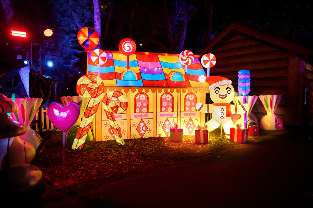 A lit up gingerbread man in front of a gingerbread house and several candies in the background