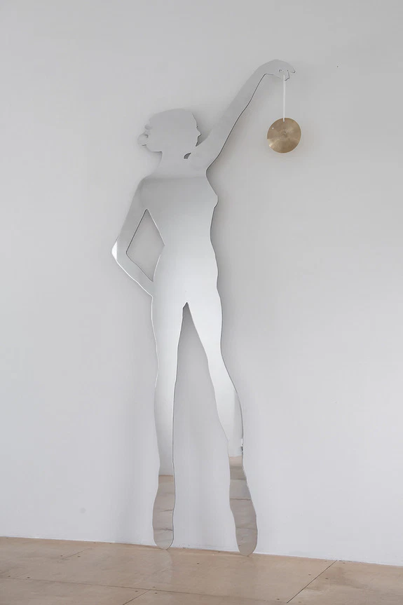 Silhouette mirror art of a ballerina on a white wall holding a round object, reflecting wooden floor.