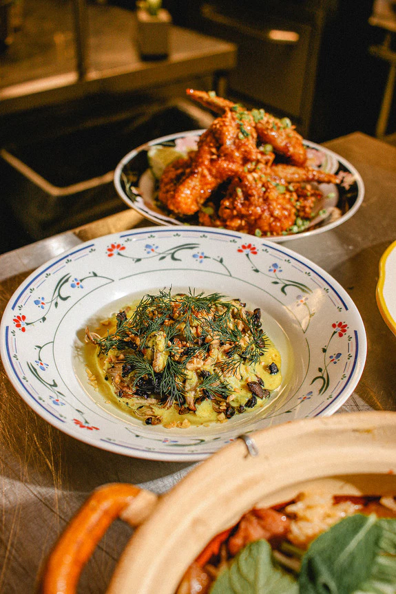 Plate of pasta topped with herbs and zucchini, surrounded by other dishes in a cozy restaurant setting.