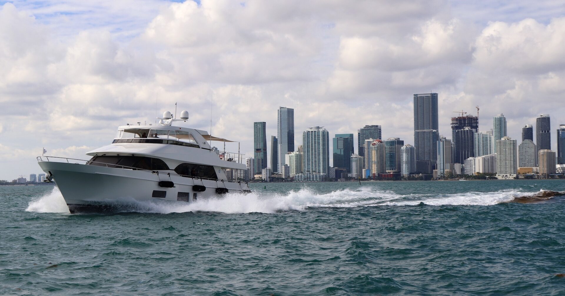 photo of a yacht cruising on the water with the Miami skyline behind it