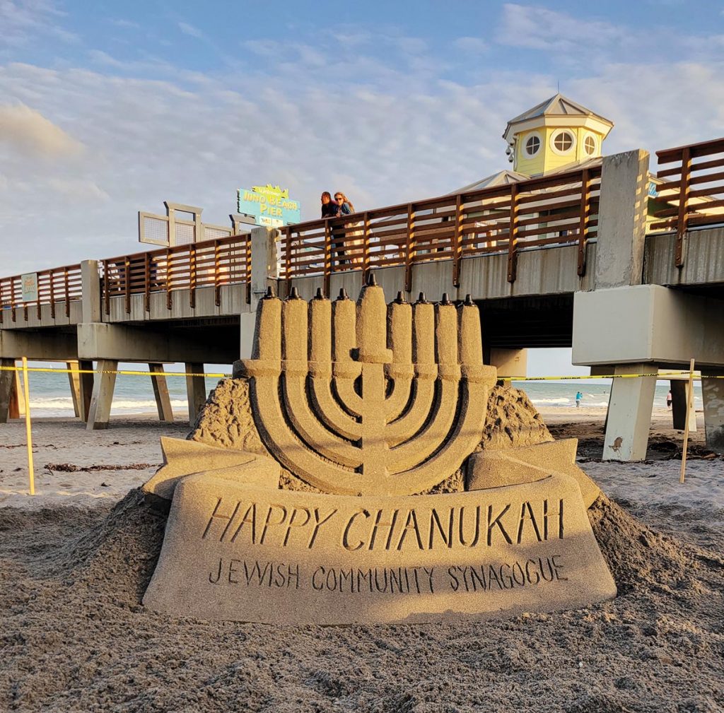 Pier-goers in Juno Beach view the Jewish Community Synagogue’s sand-sculpted menorah. Photo courtesy of The Jewish Community Synagogue